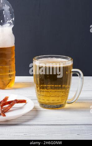 A mug of beer poured from a plastic bottle and slices of dried fish on a plate Stock Photo