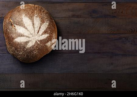 Hemp leaf print on brown bread, on wooden table background. Healthy vegetarian food. Stock Photo