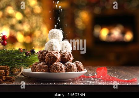 Pile of coconut and chocolate balls on Christmas with grated coconut shavings falling on top and homey background with a Christmas tree with lights an Stock Photo