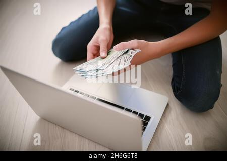 Hands with bundle of money. Teenager counts banknotes while sitting by laptop. Cash bills pouring into freelancer. Easy money earned on online exchang Stock Photo