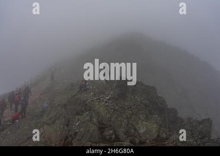 KARPACZ, POLAND - OCTOBER 16, 2021: Tourists climb Poland's popular mountain peak - Sniezka in the Giant Mountains in cloudy weather. Stock Photo