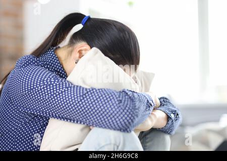 Sad woman sits on couch hiding face in pillow closeup Stock Photo