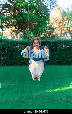 Blue-eyed caucasian older lady riding on a swing laughing and enjoying life. Concept of young spirit in older people Stock Photo