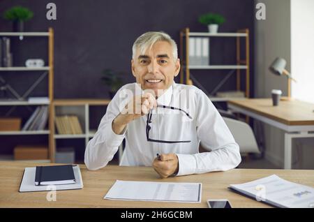 Portrait of happy senior businessman sitting at office desk and looking at camera Stock Photo