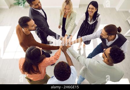 Diverse team of happy young business people standing in circle and stacking hands Stock Photo