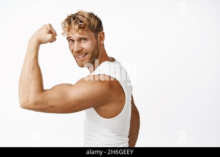 Smiling sportsman flex biceps, showing strong arm muscle, workout in gym, doing sport exercises, white background Stock Photo