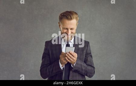Smiling businessman using smartphone standing over grey studio background Stock Photo