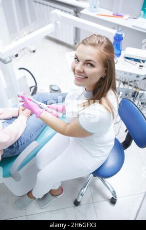 Vertical top view shot of a beautiful cheerful female dentist smiling to camera while working with patient Stock Photo