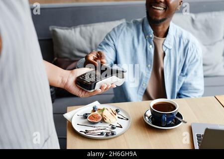 Unrecognizable young Black man sitting at table in modern cafe paying for order using his smartphone Stock Photo