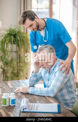 Attentive doctor supporting a depressed gray-haired man Stock Photo