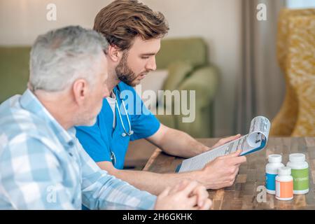 Serious geriatrician prescribing multivitamins to a gray-haired man Stock Photo
