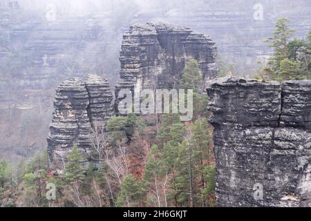 Foggy Mystical landscape Forested Mountains Shrouded In Mist And Clouds. Rocks in foggy forest among trees in Autumn. Time lapse Bohemian Switzerland Stock Photo