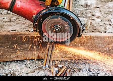 A male hand cuts off pieces of reinforcement using an angle grinder. Cutting steel interspersed with sparks on a construction site. Sparks when cuttin Stock Photo