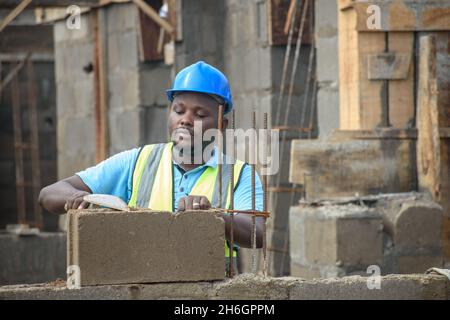 African male construction worker with helmet working with trowel on a building site Stock Photo
