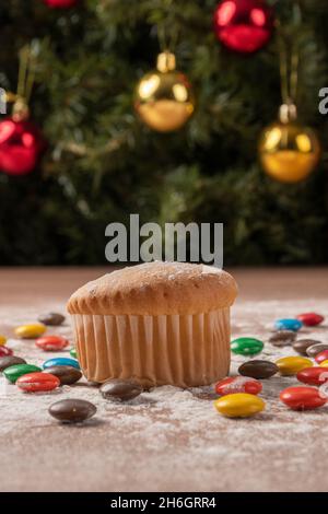 cake surrounded with several round colored chocolates with sprinkled sugar on a table, studio with food in the background a christmas tree, desserts Stock Photo