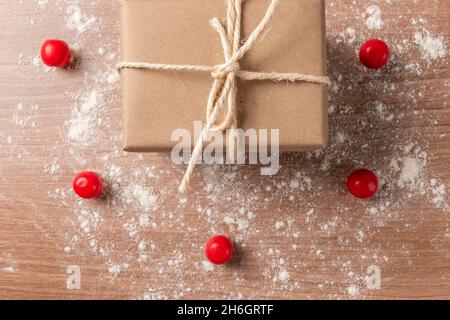 gift box wrapped in paper with a rope bow on a wooden table, decorated with red candy balls, surprise and share as wallpaper in studio Stock Photo