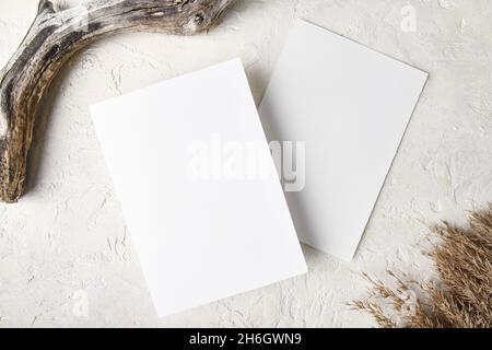 Two white invitation card mockup with boho decoration: pampas grass and piece of wood, natural eco-friendly decor, 5x7 ratio, similar to A6, A5, top v Stock Photo