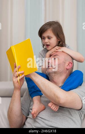 Father and son together enjoying reading and discussing school homework exercises from yellow textbook. Stock Photo