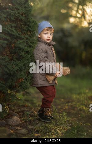 Boy with blue hat and wooden airplane toy standing in garden Stock Photo