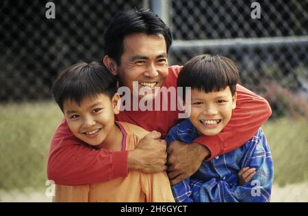 Austin Texas USA, 1995: Vietnamese-American dad hugs his young sons in the family's backyard. MR EC-131-132  ©Bob Daemmrich Stock Photo