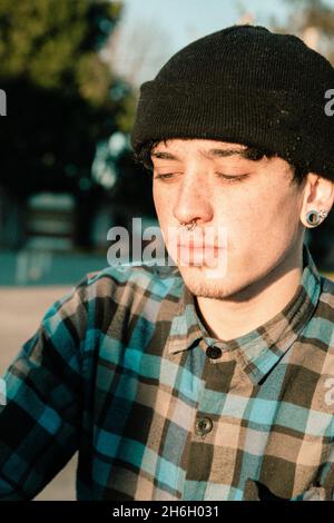 Portrait of a Caucasian male teenager wearing a black beanie hat with ear and nose piercings Stock Photo