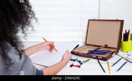 A young female African-American artist sitting on desk painting on notebook at art studio. copy space Stock Photo