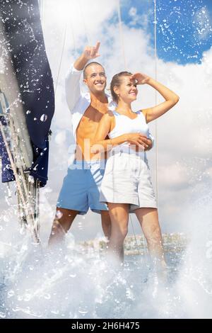 Loving couple standing on deck of sailboat during sea trip along Stock Photo