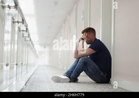 Upset man sitting on floor in hallway Stock Photo