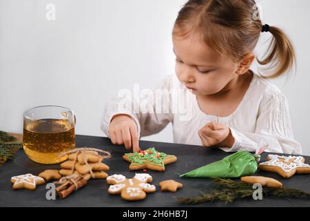 Child cooking and eating home made gingerbread cookies, stars, man. Happy toddler girl celebrated Christmas eve at home, Kid decorating pastry with Stock Photo