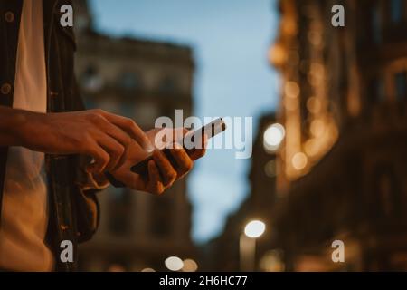 Close-up of male hands with smartphone. Night street on background. Man with mobile phone outdoors. Stock Photo