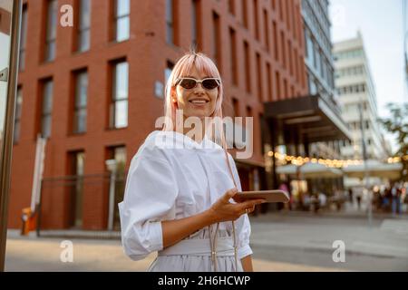 Cheerful woman standing on the street and holding smartphone Stock Photo