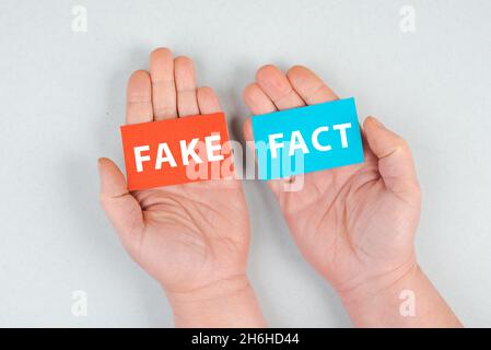 The words fake and fact are standing on blue and red colored paper, hands holding the message, news, truth Stock Photo