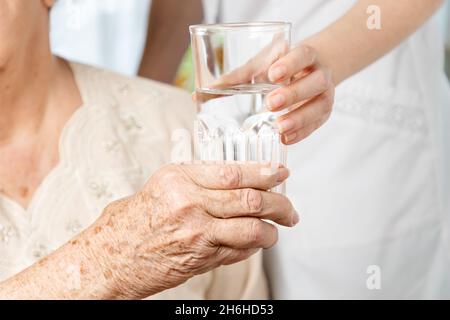 International Day of Older Persons. A nurse gives a glass of water to an elderly woman. Close up of hands. Care for the elderly in nursing homes. Stock Photo