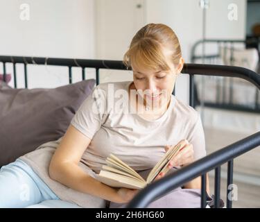 Young woman lying on bed and reading book. Social media detox and gadget free day Stock Photo