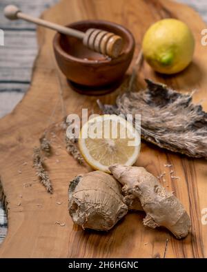 Composition of ginger roots, lemons, and honey with honey spreader, on a wooden cutting board Stock Photo