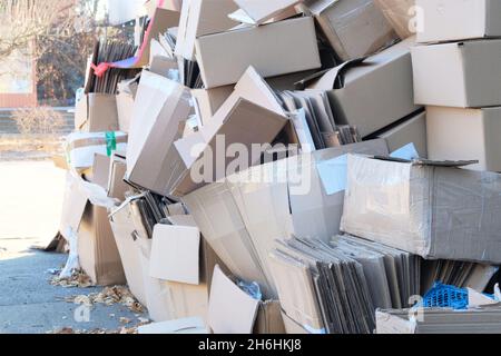 Cardboard and waste paper is collected and packaged for recycling in city in sunny day. Pile of cardboard is sorting for recycled. Stock Photo