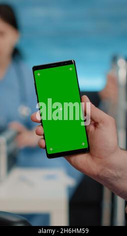 Close up of nurse vertically showing phone with green screen to senior patient living in nursing home. Medical specialist holding smartphone with chroma key and isolated mockup template Stock Photo