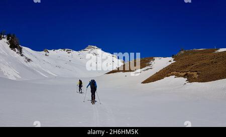 Ski mountaineer friends hiking up a summit in the Austrian Alps on a sunny winter day. Vorarlberg, Austria. Stock Photo