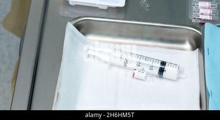 A used syringe and an empty glass ampoule opened lie in a metal cuvette. Selective focus. Stock Photo