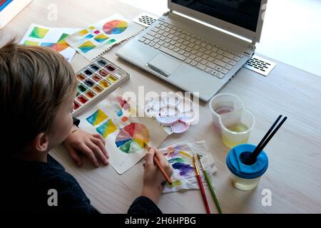 Boy painting pictures with watercolor paints during art lesson. Pupil on drawing with brush. Watercolor color wheel and palette. Color theory beginner Stock Photo