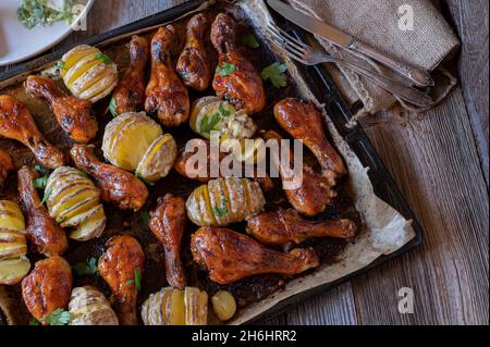 Oven baked barbecue chicken drumsticks with cheesy hasselback potatoes on a baking tray Stock Photo