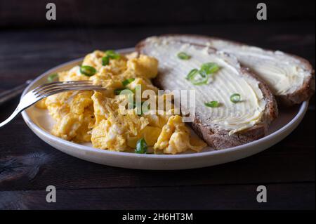 Plate with scrambled eggs and bread isolated on wooden table Stock Photo