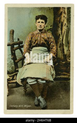 Original Edwardian tinted studio portrait postcard of Colliery Girl, Wigan (Lancashire, England, U.K.) wearing trousers and an apron, circa 1905. Stock Photo