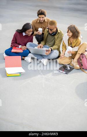 Students watching something on laptop on asphalt Stock Photo
