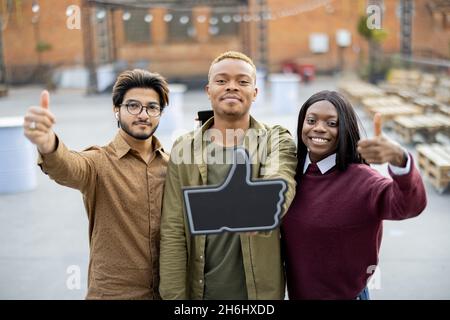 Guy hold phone and show thumb up with friends Stock Photo