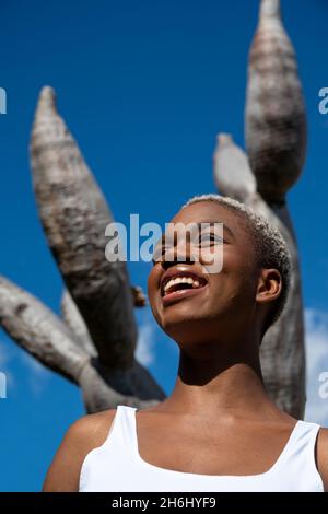 Low angle of delighte black female with short hair laughing and looking away on background of dragon tree in park Stock Photo