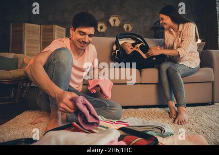 Photo of daddy put clothes baggage bag mommy play daughter baby car seat want weekend resort abroad departure evening late indoors Stock Photo