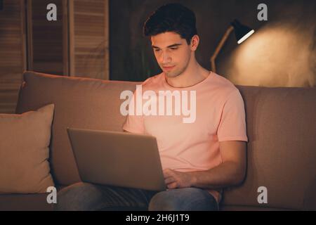 Portrait of attractive focused guy sitting on divan using laptop preparing report late night at home house flat indoors Stock Photo