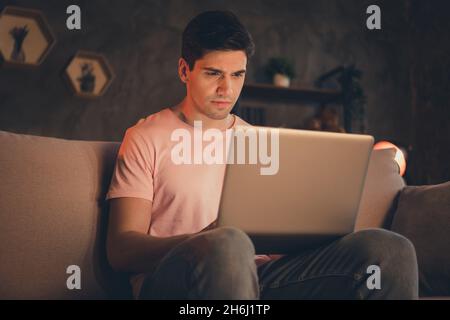 Portrait of attractive focused serious guy sitting on divan using laptop writing report over time sleepless night at home indoors Stock Photo
