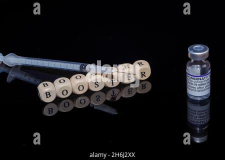 Bamberg, Germany - 16.11.2021. Letter cubes form the word booster, BioNTech-Pfizer Comirnaty original vial and syringe Stock Photo